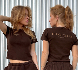 Brown t-shirt with 'dipped in dolce' on front and 'Dolce Glow by Isabel Alvia' text on back and back worn by a person.