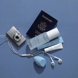 Dolce Glow travel bundle includes Acqua face mist. self tanning contour, vanilla lip butter and blending sponge. Canon camera, passport, and earbuds also in image on a blue background.