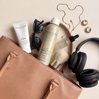 Open brown handbag containing Dolce Glow travel self-tanning products, sunglasses, a necklace, earrings, and headphones on a beige background.