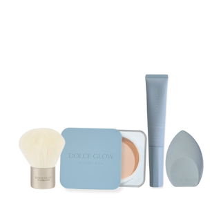 Dolce Glow Travel Bundle products including SPF50 Body Balm, tanning contour, brush, and blending sponge on a sandy beach with mesh bag.